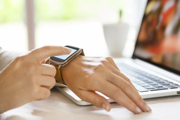 Mujer sincronizar su reloj inteligente con el ordenador portátil . — Foto de Stock