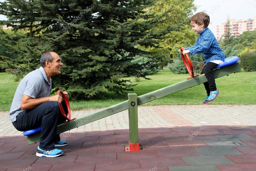 Happy family enjoying seesaw at the playground in the park Stock