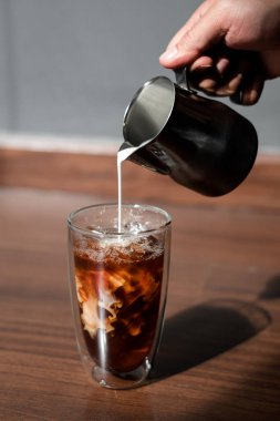 Barista bir bardak buzlu kahveye süt dolduruyor.