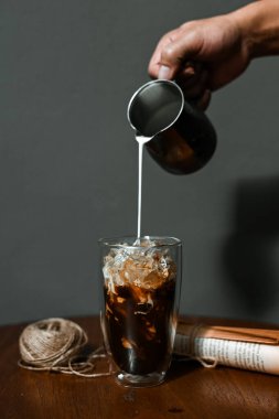 Barista bir bardak buzlu kahveye süt dolduruyor.