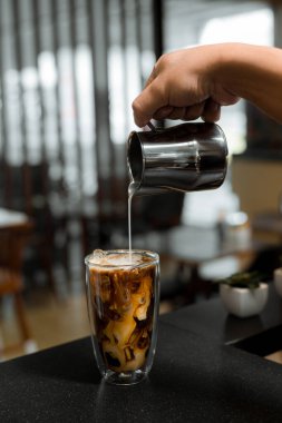 Barista bir bardak buzlu kahveye süt dolduruyor.
