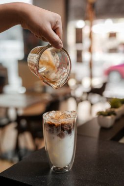 Barista bir bardak buzlu kahveye süt dolduruyor.