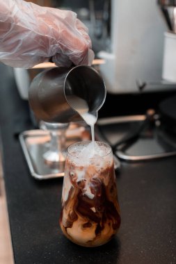 Barista bir bardak buzlu kahveye süt dolduruyor.