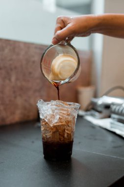 Barista bir bardak buzlu kahveye süt dolduruyor.
