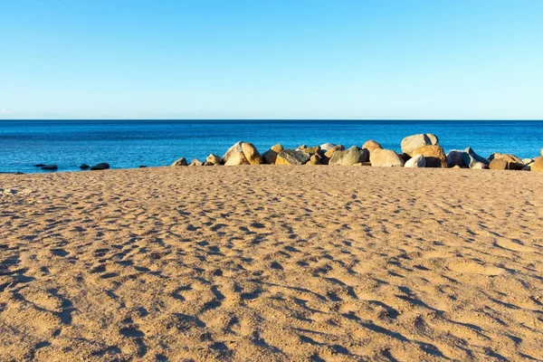 Písečná pláž a velké kameny na břehu u vody — Stock fotografie