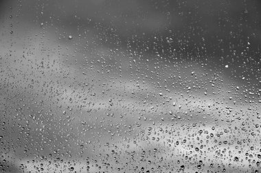 water drops from rain on glass in a blurry cloud sky for an abstract textured background monochrome tone