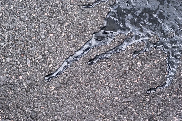 Black bitumen abstract form on damp speckled asphalt — Stock Photo, Image