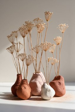 Güneş ışığında kurumuş kır çiçekleriyle el yapımı kil vazolar. Sıcak toprak tonları ve Wabi Sabi zarafeti ile doğal durgun yaşam.