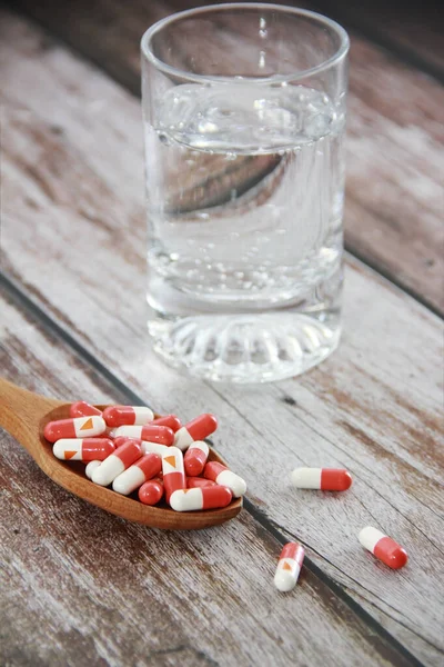 Röda läkemedelskapslar i en sked och ett glas vatten — Stockfoto
