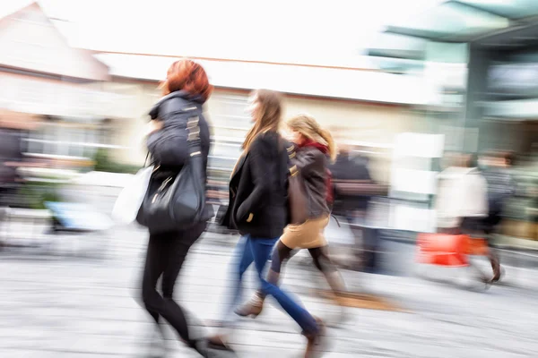 Young women walking against shop window at dusk, zoom effect, mo — Stock Photo, Image