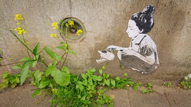 Brüksel, Belçika - 13 Mayıs 2018: Vahşi çiçekleri sulayan kız. Cheval Noir Sokağı 'ndaki sanat eseri.