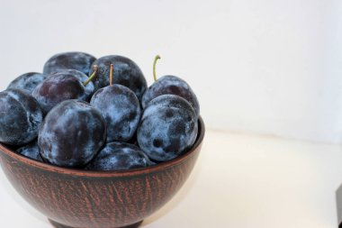 Beyaz bir zemin üzerinde, derin bir kil plaka içinde birkaç olgun mavi erik ve bir kopya alanı.