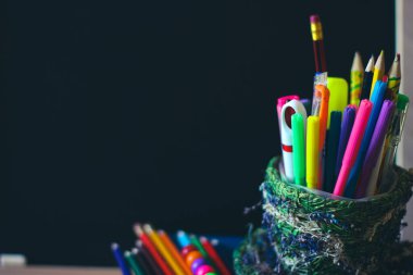 Karanlık okul tahtasının arka planında renkli kalemler ve kalemler var. Kopya alanı için pano yerinde.