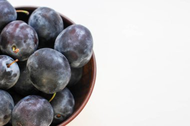 Beyaz bir zemin üzerinde, derin bir kil plaka içinde birkaç olgun mavi erik ve bir kopya alanı.