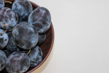 Beyaz bir zemin üzerinde, derin bir kil plaka içinde birkaç olgun mavi erik ve bir kopya alanı.