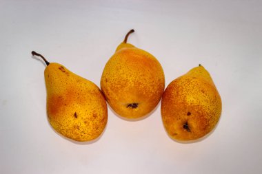 Beyaz arka planda duran üç sarı armut.