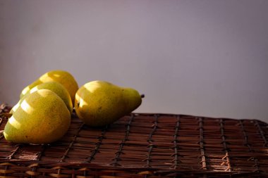 Güneş ışınlarıyla aydınlatılmış hasır bir sepetin üzerinde birkaç olgun sarı armut duruyor.
