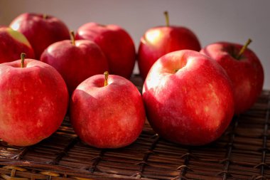 Güneş ışınlarıyla aydınlatılmış hasır bir sepetin üzerinde birkaç olgun kırmızı elma duruyor.