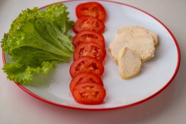 Lezzetli diyet kahvaltısı, salata yaprakları, dilimlenmiş domates ve haşlanmış tavuk göğsü.