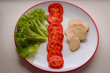Lezzetli diyet kahvaltısı, salata yaprakları, dilimlenmiş domates ve haşlanmış tavuk göğsü.