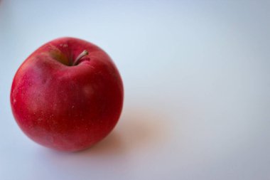 Beyaz bir yüzeyde kırmızı elma duruyor.