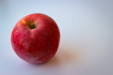 Beyaz bir yüzeyde kırmızı elma duruyor.