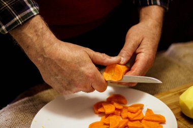 A man cuts ripe carrot into slices to make soup