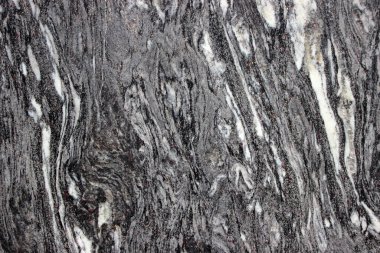 Görünür katmanları ve doğal dikey çatlağı olan koyu bir kaya yüzeyinin detaylı dokusu. Soyut jeolojik arkaplan taş deseni ve yapıyı gösteriyor.