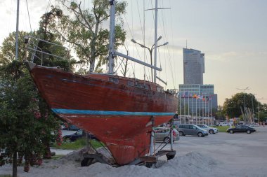 5 Haziran 2019 'da Polonya' nın Gdynia kentindeki yat limanına yanaşan eski bir ahşap yat. Arka planda, modern Deniz Kuleleri binası ve ulusal bayraklar akşam ışığında görülebilir..