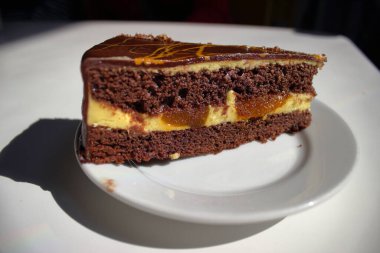 Çikolatalı pasta dilimini kremalı ve karamel dolgulu kapayın beyaz tabakta gün ışığında servis edilen tatlı ve yiyecek kavramını yaratın..