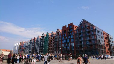 Gdansk, Polonya. Haziran 07, 2019. İnsanlar güneşli bir günde tarihi tahıl ambarları ve modern binalarla Motlawa Nehri boyunca nehir kenarındaki gezinti alanında toplandılar..