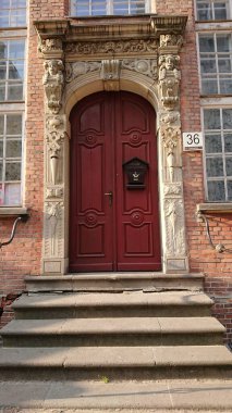 GDANSK, POLAND - 07 Haziran 2019: Tarihi kırmızı ahşap bir giriş kapısı son derece dekoratif taş bir kapı çerçeveli Eski Şehir 'deki taş basamaklar da dahil olmak üzere heykeller ve kabartmalar.