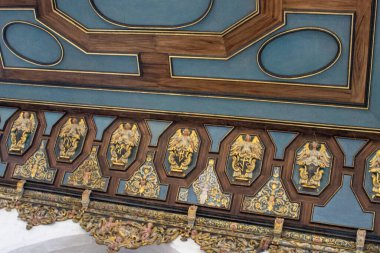 Süslü barok tavan detayı altın meleklerle süslenmiş ve tarihi kilise içinde ahşap süslemeler, zengin renkler ve simetri.