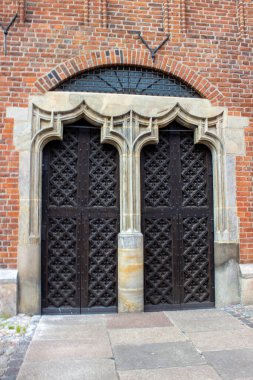 Tarihi tuğla duvara yerleştirilmiş simetrik gotik ahşap kapılar. Eski Avrupa mimarisinin dış yüzeyinde taş kemer detaylarıyla birlikte..