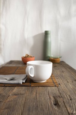 Beyaz seramik bardak, kaşık ve besin malzemeleri ahşap bir masa üzerinde bir plasemat ile