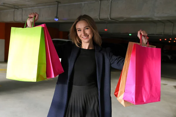 A young woman happy after shopping stands in the parking of a shopping center