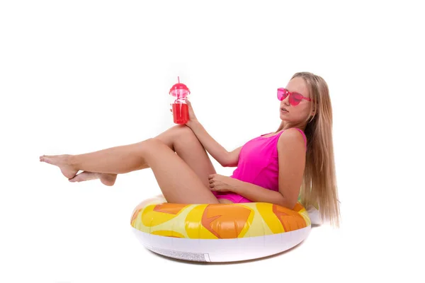 一位身穿粉色泳衣和眼镜的年轻女子躺在一个充气的泳圈上 喝着柠檬水 — 图库照片