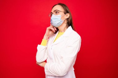 Beyaz önlüklü ve koruyucu maskeli genç bir kadın doktor.