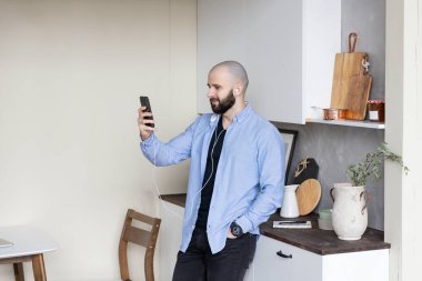 Mavi gömlekli ve siyah kotlu bir adam evdeki video bağlantısıyla telefonda. Serbest çalışma kavramı.