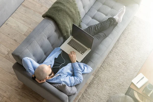 The guy is lying on the couch and working on a laptop. The concept of working from home