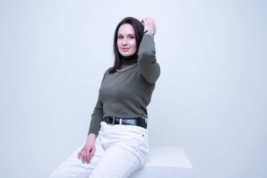 Koyu golf ve açık renk kot giyen esmer bir kadın stüdyoda poz veriyor.