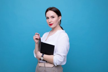 Mavi arka planda günlüğü ve kalemi olan esmer bir kadın.