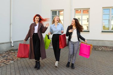 Renkli çantalı üç genç kadın alışveriş yaptıktan sonra yürür.
