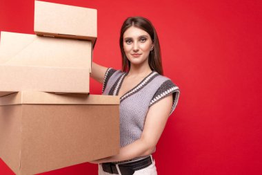 Kırmızı arka planda karton kutular tutan genç bir kadın.