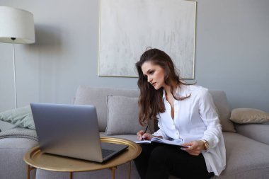 Genç bir kadın kanepede oturuyor ve evde internetten çalışıyor.