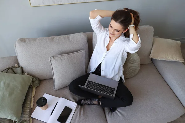 Genç Bir Kadın Kanepede Oturuyor Evinde Dizüstü Bilgisayarla Çalışıyor — Stok fotoğraf