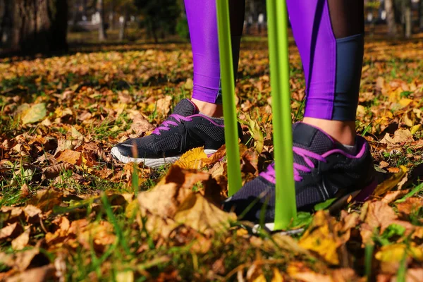 Close-up of the feet of a girl in sneakers who trains with an elastic band in a park