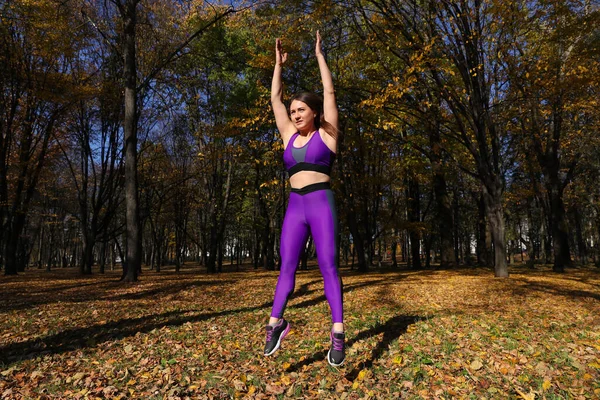 A girl with a tracksuit jumps in the park. Exercise in the fresh air
