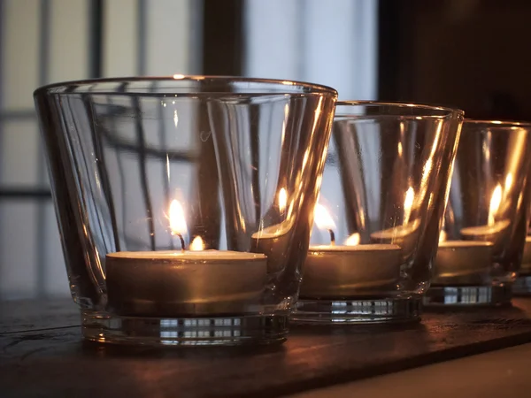 Lit candles in glasses on rustic wooden shelves — Stock Photo, Image