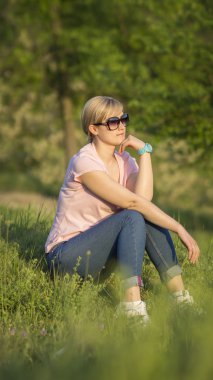 Yeşil çimenlerin üzerinde oturan ve bir şey düşünme bir genç whitehair kadın